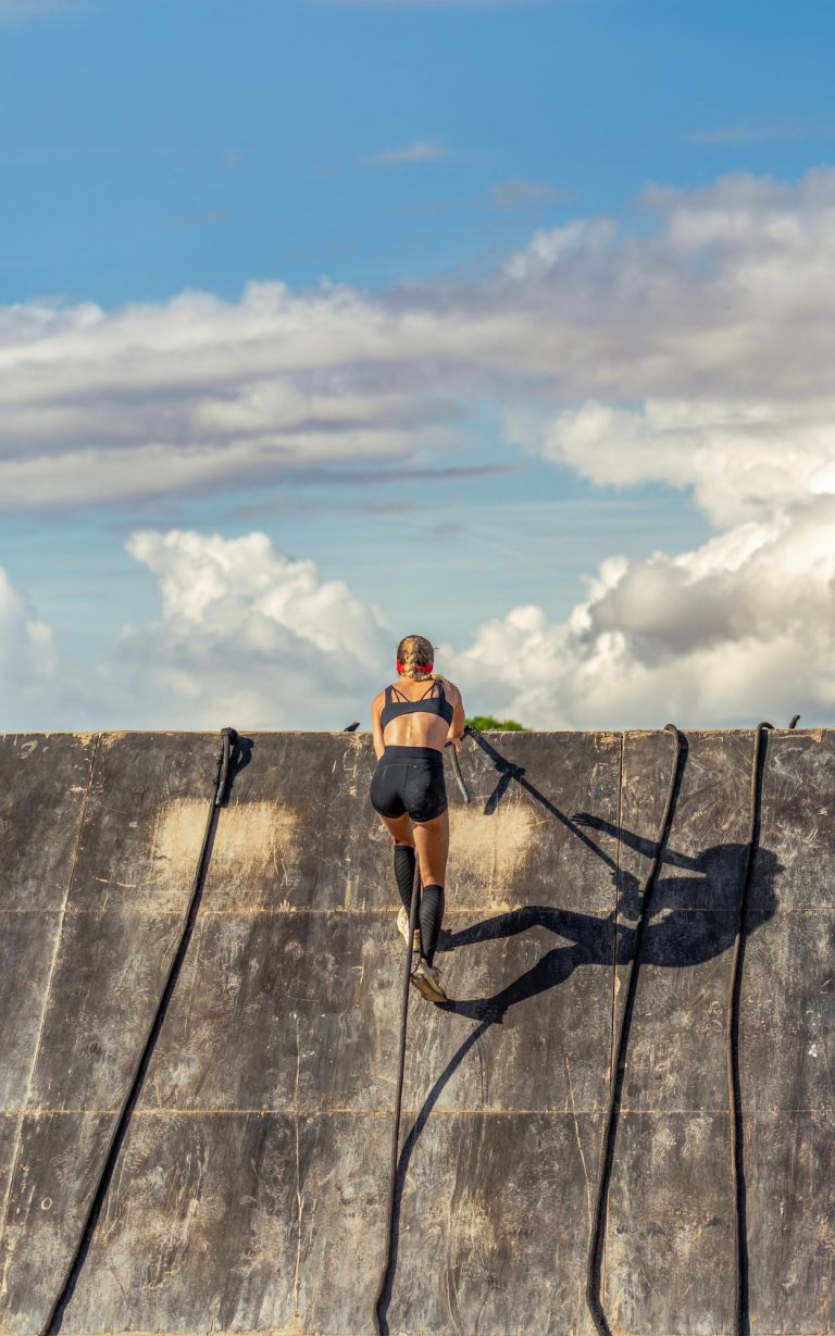 Female athlete climbing a wooden obstacle wall in an OCR race