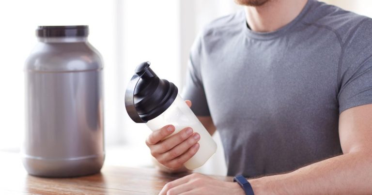 Athlete preparing sports supplement shake with protein jar and shaker bottle