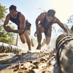 Athletes crawling through muddy obstacle course logs during an OCR race