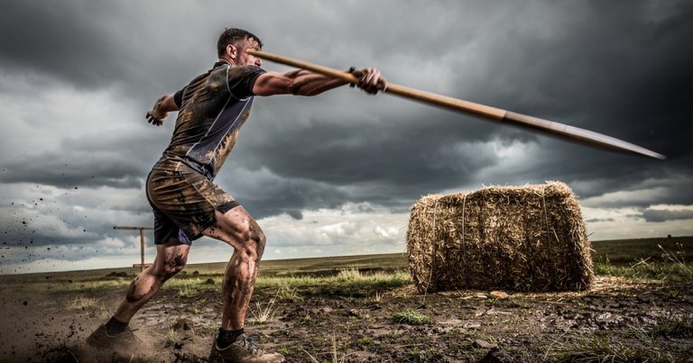 OCR athlete throwing spear at hay bale target on race course