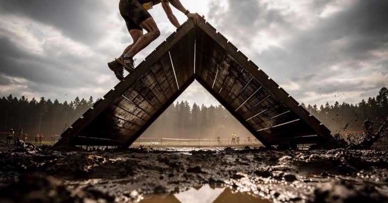 OCR athlete cresting a muddy wall obstacle at a race