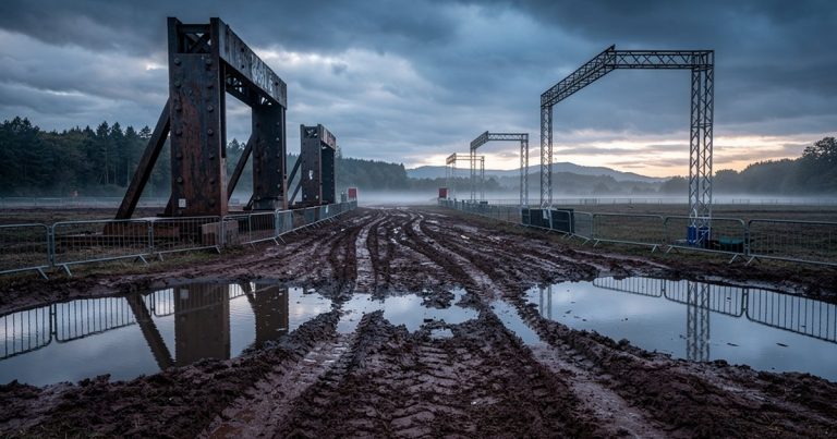 Empty OCR race venue with steel obstacles and water pits under dramatic storm clouds