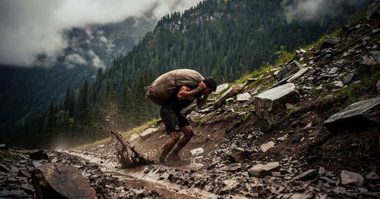 Athlete hauling a sandbag up a steep muddy hillside on a Spartan Beast course