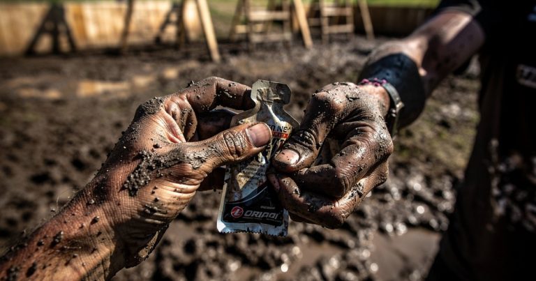 Muddy hands trying to open an energy gel packet during a long OCR race