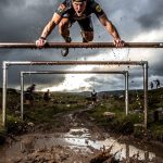 OCR athlete crossing monkey bars on a muddy obstacle course race