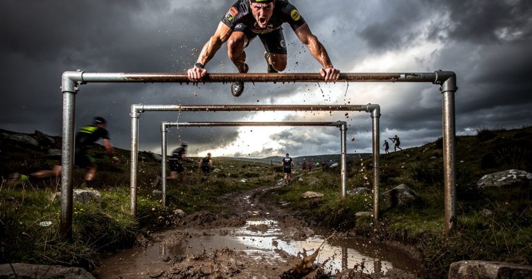 OCR athlete crossing monkey bars on a muddy obstacle course race