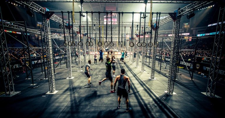 Indoor stadium obstacle course racing setup with rigs and structured obstacles under dramatic arena lighting