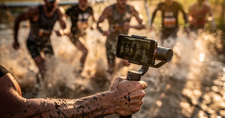 OCR athlete filming race footage on a gimbal-mounted smartphone during an obstacle course event