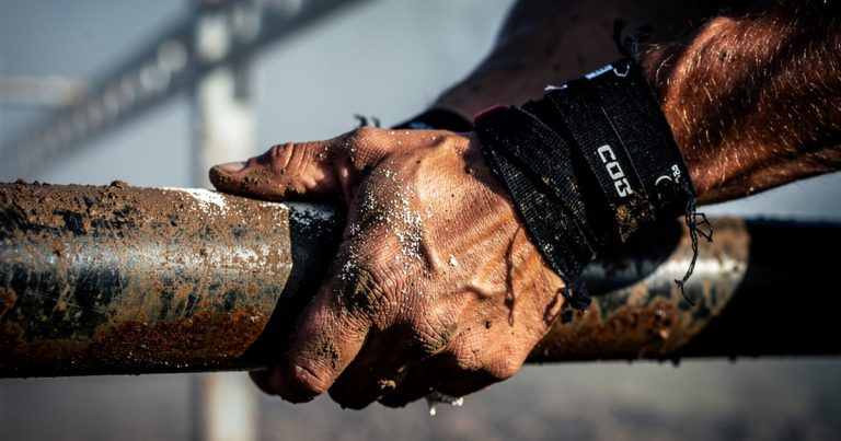 OCR athlete gripping a rig obstacle with chalk-covered hands and taped wrists