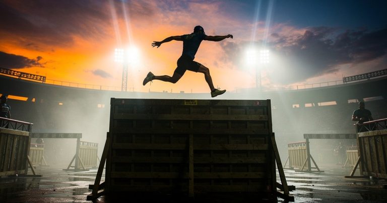Silhouetted athlete leaping over a wall obstacle at an international OCR championship event