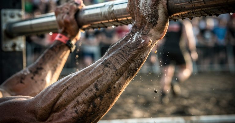OCR athlete gripping a rig obstacle with forearm endurance on a race course
