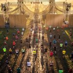 Aerial view of hundreds of athletes at an OCR race start line stretching across a vast outdoor course