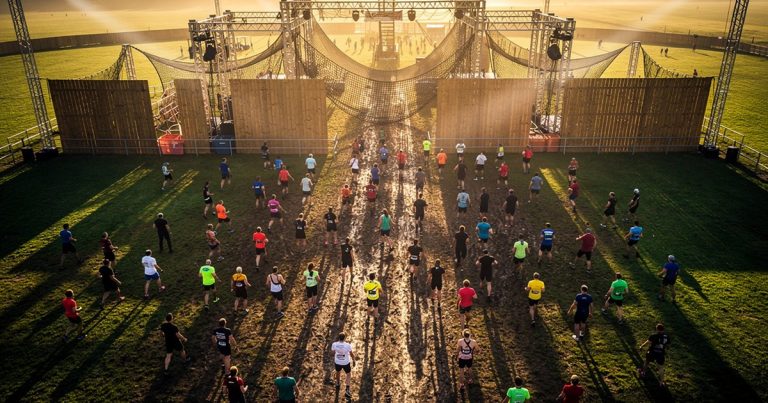 Aerial view of hundreds of athletes at an OCR race start line stretching across a vast outdoor course