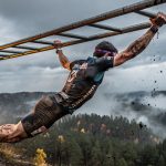 OCR athlete gripping monkey bars on race course in dramatic outdoor lighting