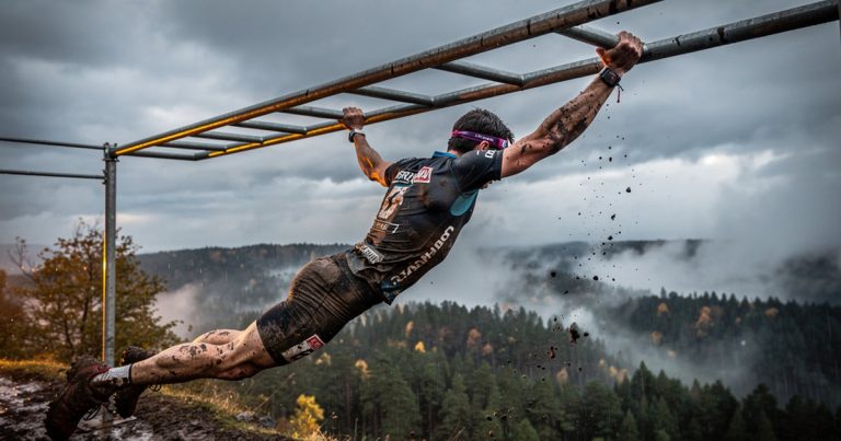 OCR athlete gripping monkey bars on race course in dramatic outdoor lighting